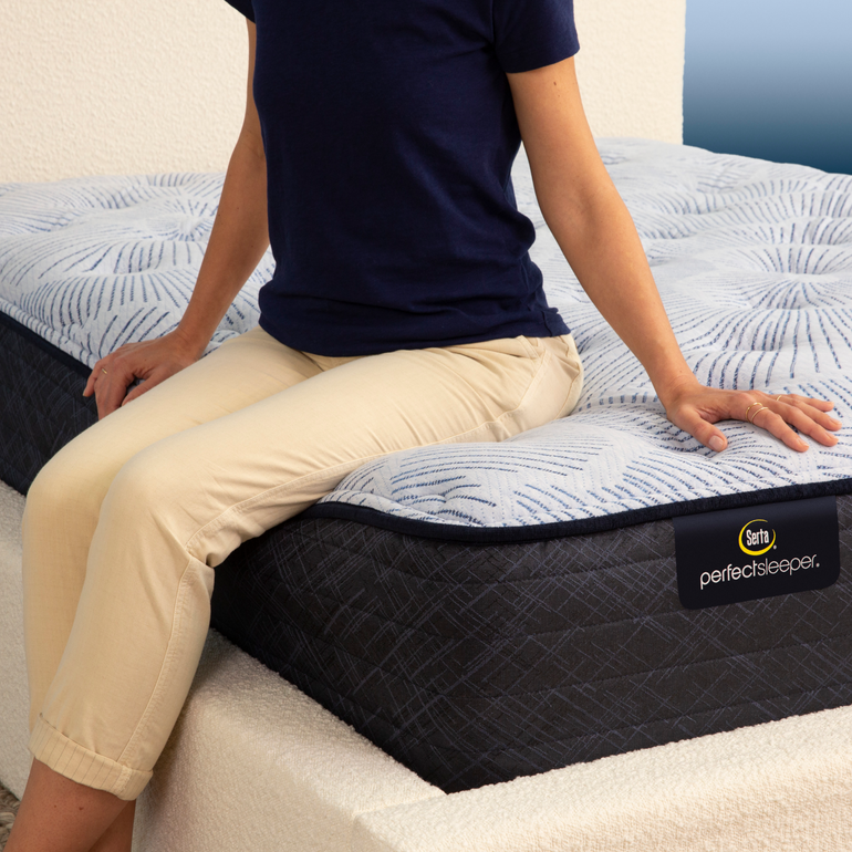 Person sitting on bed to show firmness level of Serta Perfect Sleeper plush mattress||feel: plush||level: enhanced