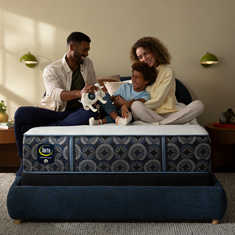 Family of 3, man, woman and boy sitting on top of a Serta Perfect Sleeper mattress with a Serta sheep