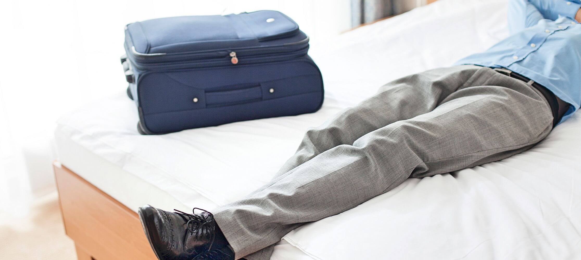 Man relaxing with suitcase on bed