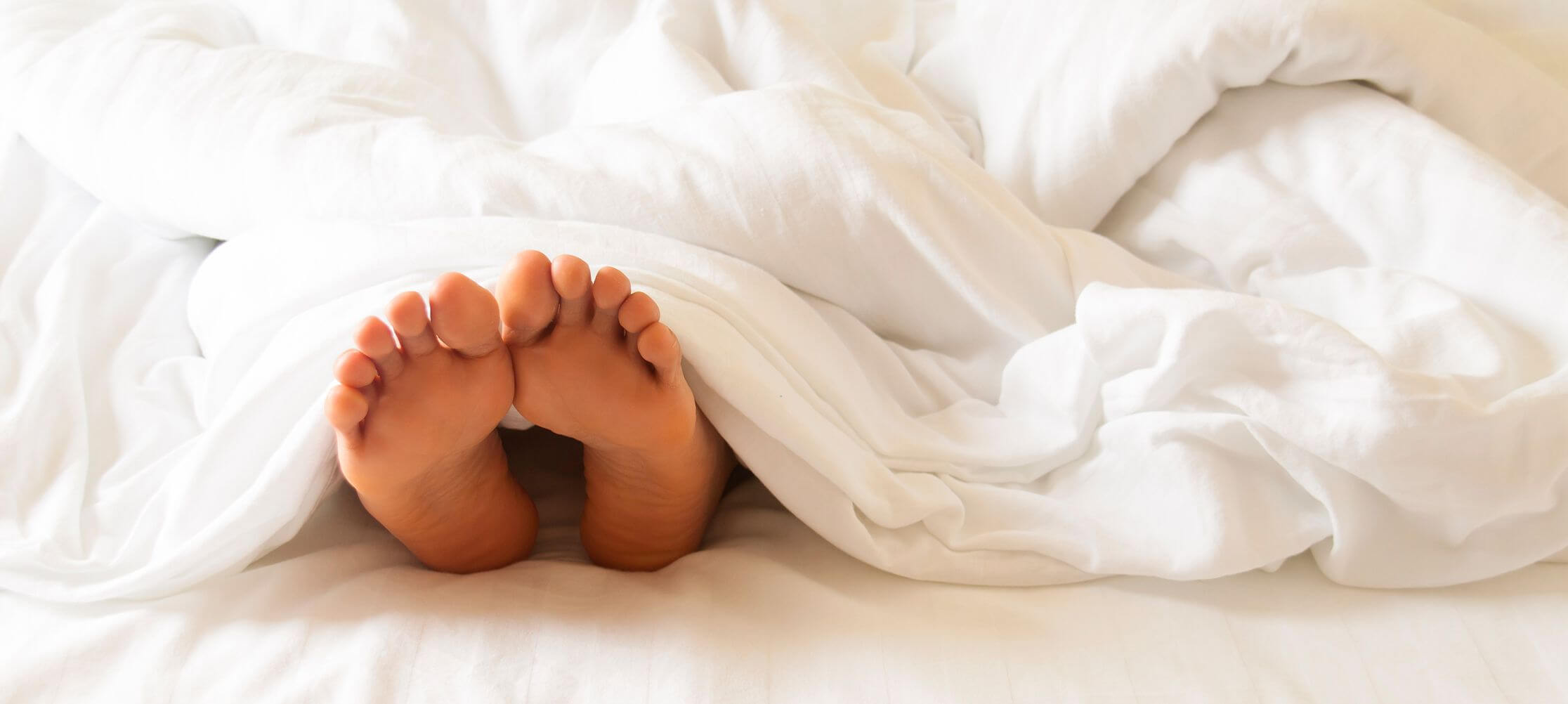 Bare feet under soft white bedding