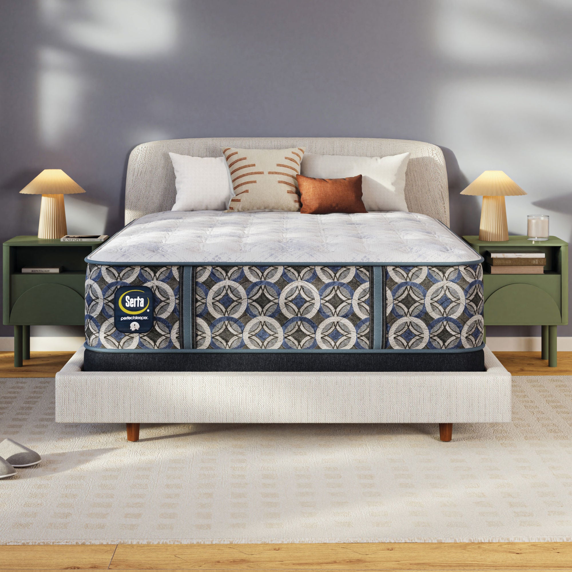 A Serta perfect sleeper plush mattress with a pattern matching upholstered base in a styled bedroom scene, with two green nightstands, lamps, pillows, and a gray wall.