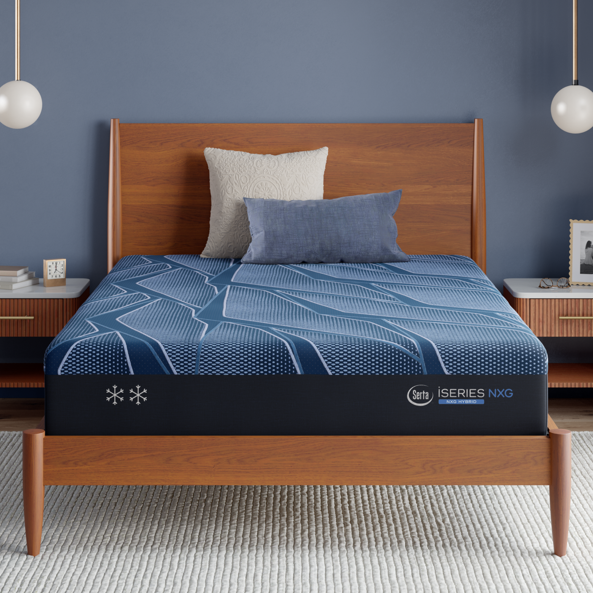 A Blue Serta® iSeries® NXG™ Mattress on a wooden bed frame in a styled bedroom setting, with a blue patterned bedding cover, two pillows, side tables, pendant lights