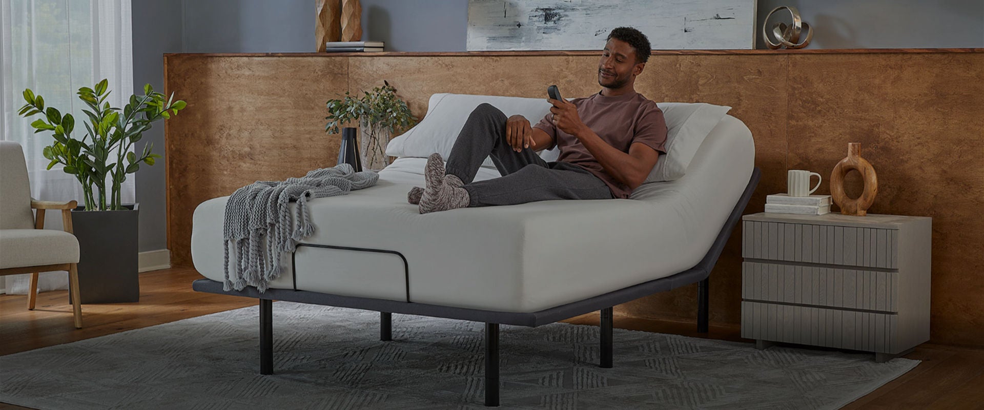 A man sitting on a Serta mattress, sitting on a baselogic adjustable base. The man is holding the remote with a smirk on his face as he looks at the settings.