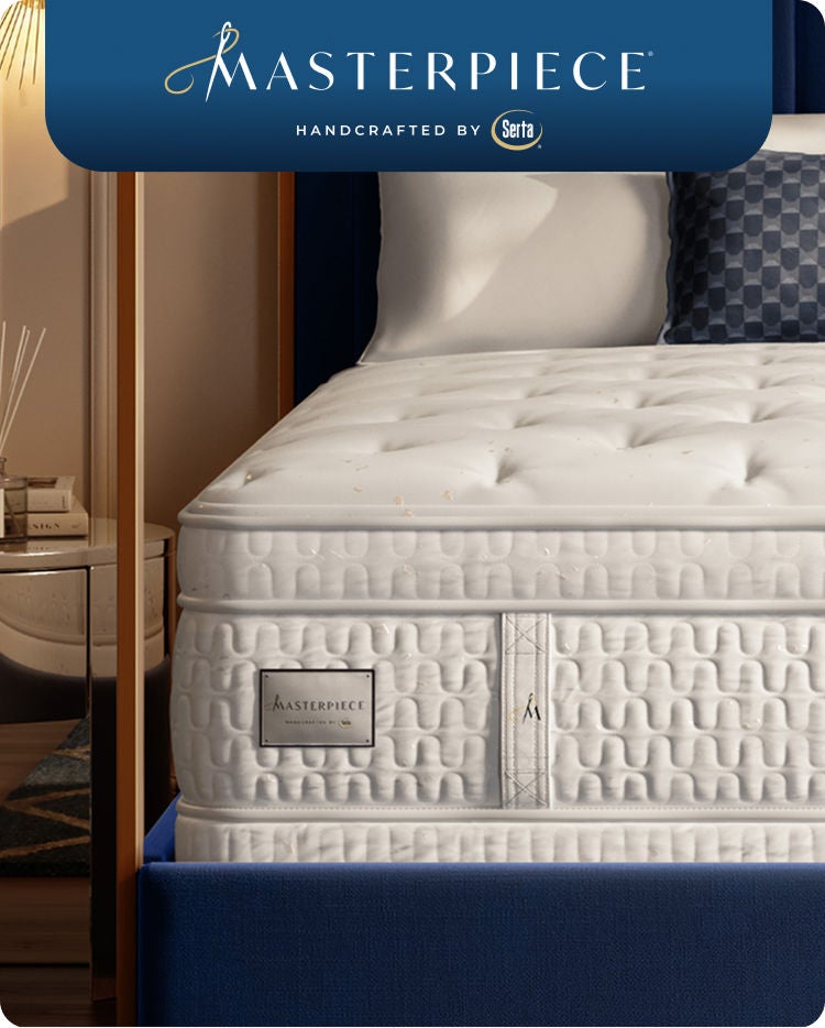Corner of a Serta Masterpiece mattress in a brown bedframe with 3 pillows on top of it.