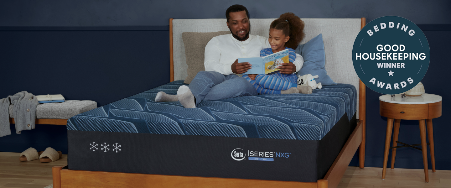 Father and Daughter reading a book while sitting on top of a Serta iSeries NXG mattress sitting in a brown wood bedframe with 2 pillows on top of it. With a "Bedding Awards Winner Good Housekeeping Winner" Circular stamp in the top right corner