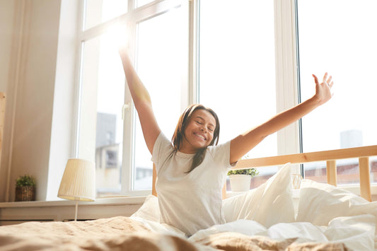 Happy woman stretching in bed with sun rising behind her.