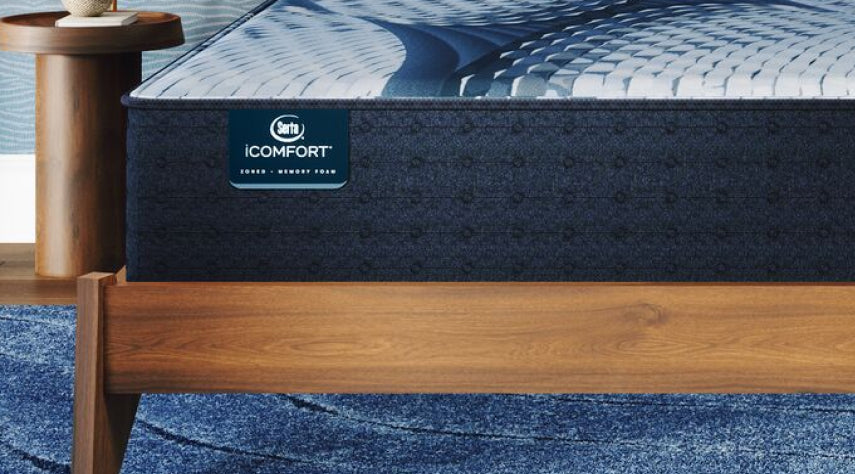 Corner of a Serta iComfort mattress sitting in a brown bed frame on a blue carpet