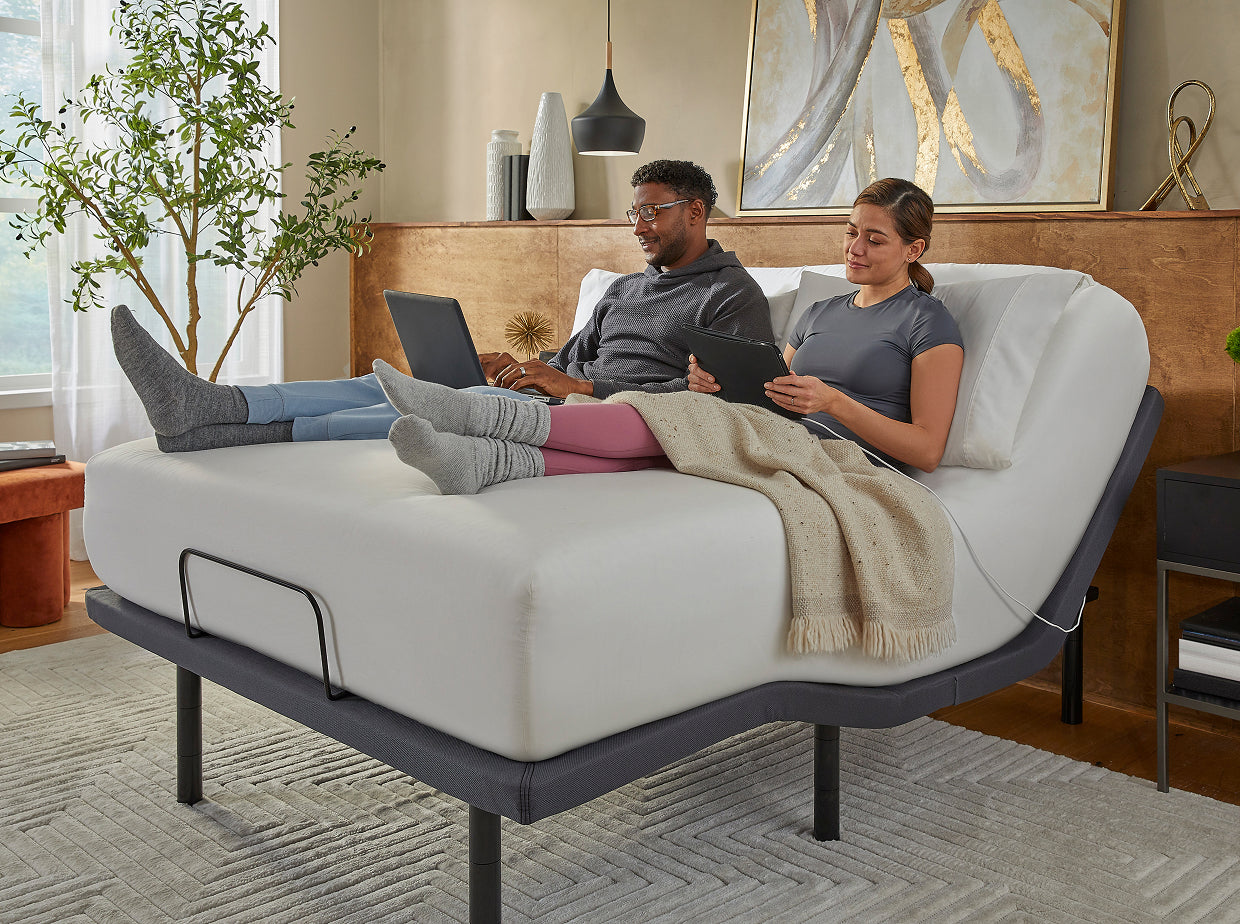 Man and woman looking at their tablets sitting on a white mattress that is on a baselogic adjustable frame.