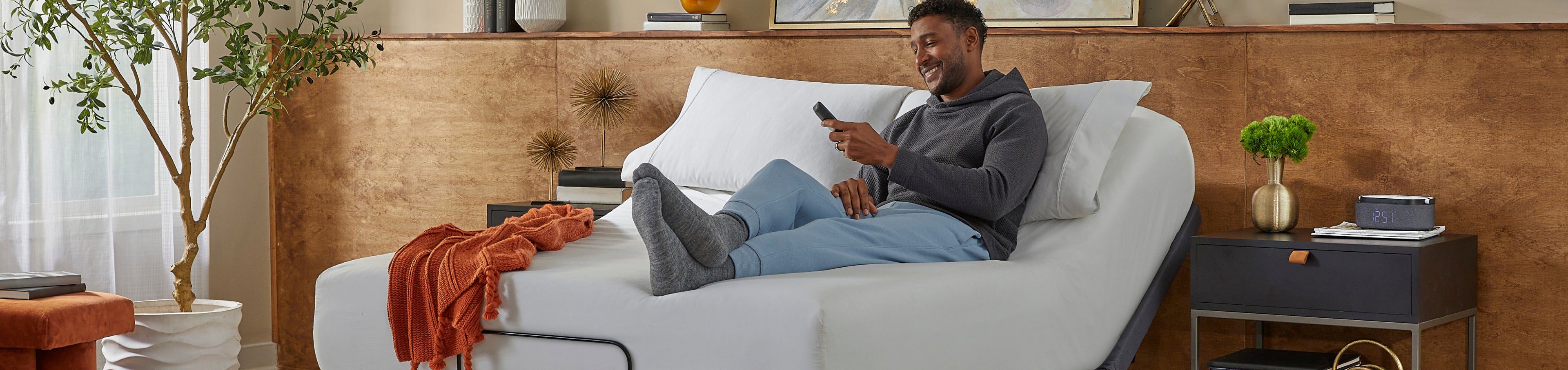 Man laying on a white mattress in a gold baselogic adjustable base olding the remote