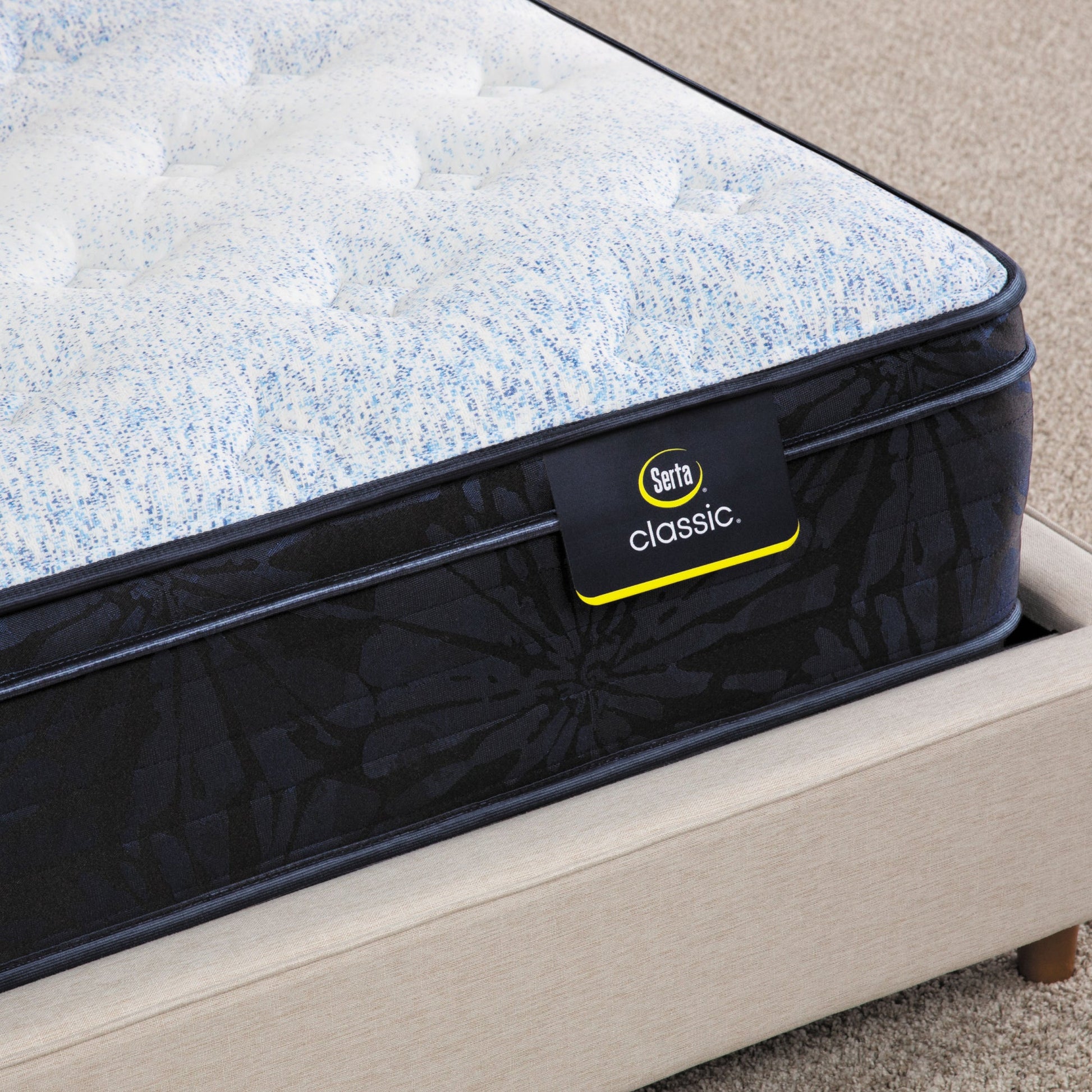 Corner of Serta classic dorian plush euro top mattress sitting in a beige bed frame ||feel: plush euro top ||level: standard