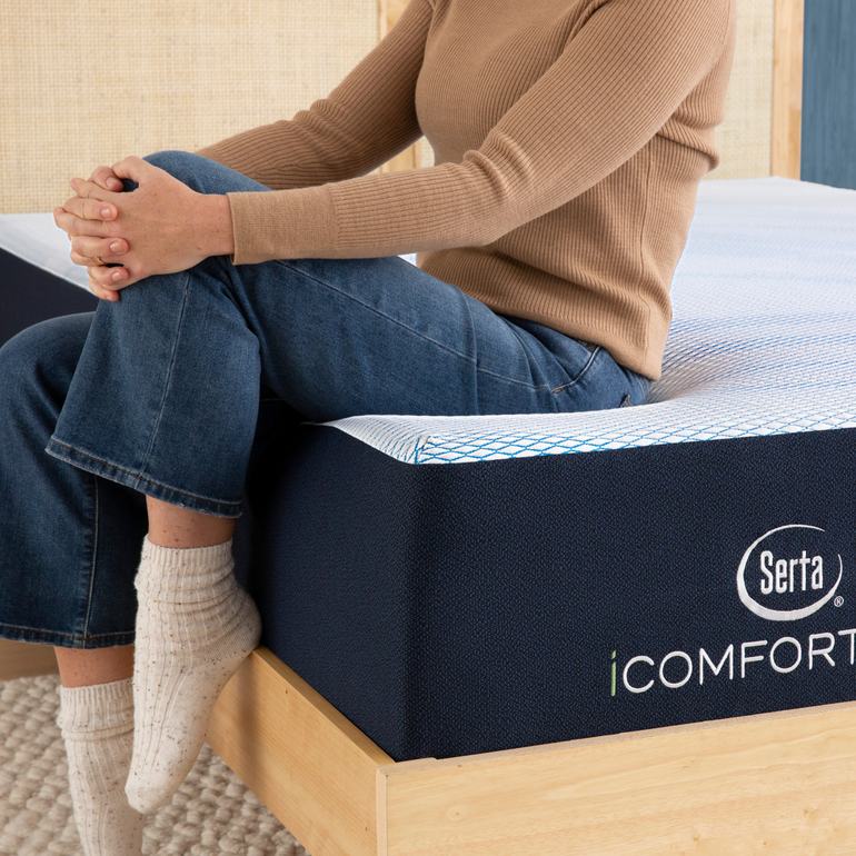 Person sitting on bed to showcase firmness level of Serta iComforteco mattress||feel: plush||level: standard