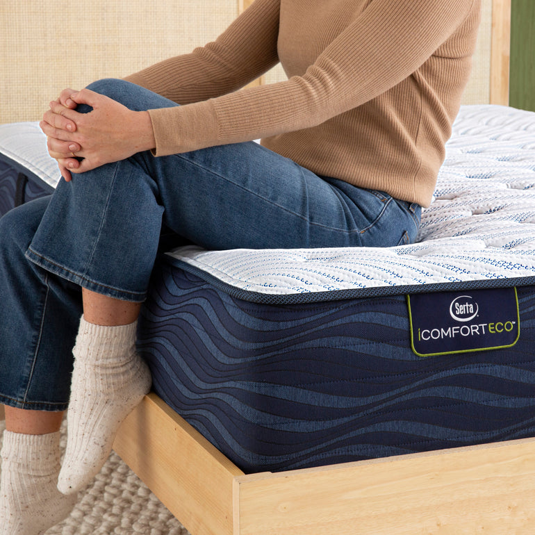 Person sitting on bed to showcase firmness level of Serta iComforteco medium mattress ||feel: medium||level: standard