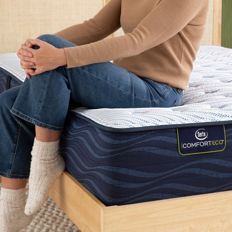 Person sitting on bed to showcase firmness level of Serta iComforteco firm mattress ||feel: extra firm||level: standard