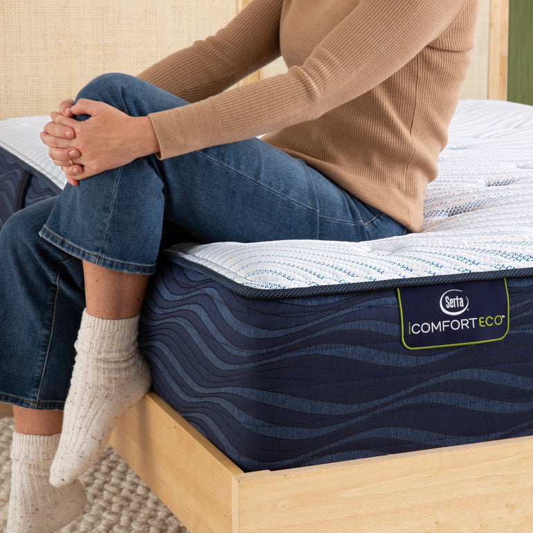 Person sitting on bed to showcase firmness level of Serta iComforteco plush mattress ||feel: plush||level: standard