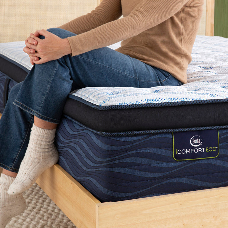 Person sitting on bed to showcase firmness level of Serta iComforteco firm pillow top mattress ||feel: firm pillow top||level: standard