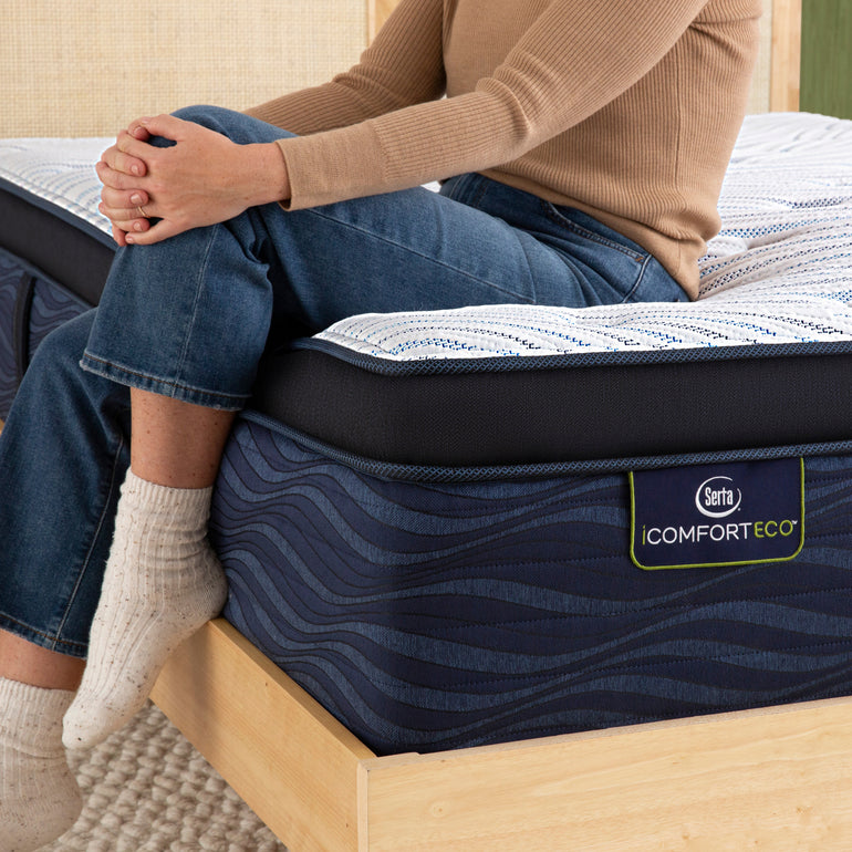 Person sitting on bed to showcase firmness level of Serta iComforteco ultra plush pillow top mattress ||feel: ultra plush pillow top||level: ultimate