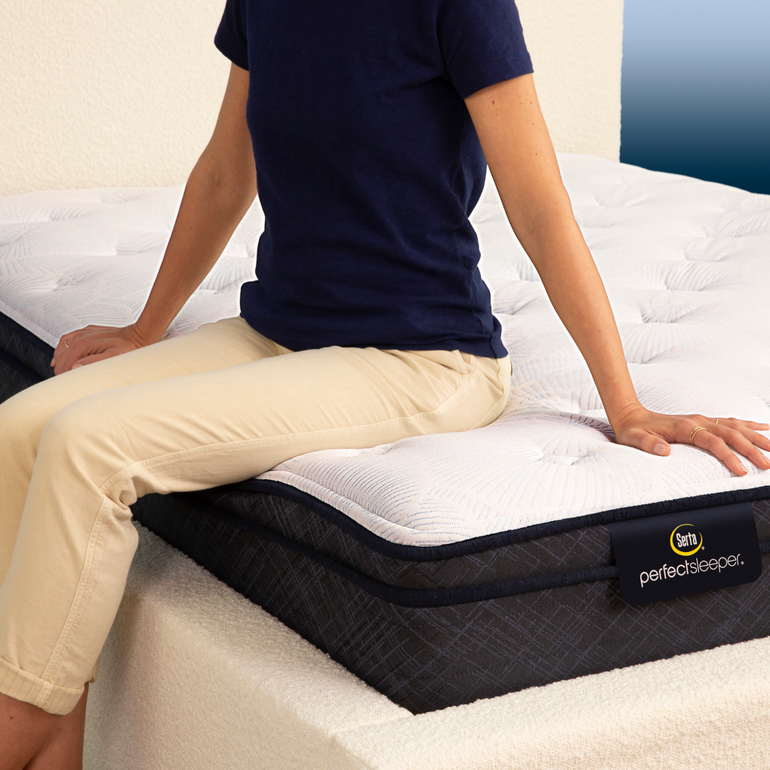 Person sitting on bed to show firmness level of Serta Perfect Sleeper plush euro top mattress||feel: plush euro top||level: standard