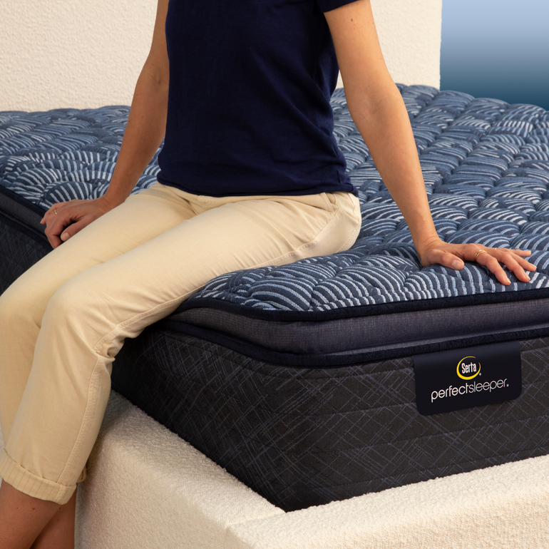 Person sitting on bed to show firmness level of Serta Perfect Sleeper firm pillow top mattress||feel: firm pillow top||level: ultimate