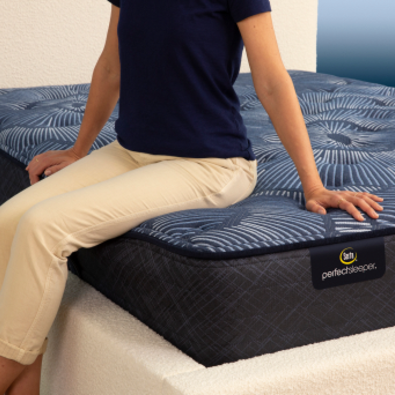 Person sitting on bed to show firmness level of Serta Perfect Sleeper plush mattress||feel: plush||level: ultimate