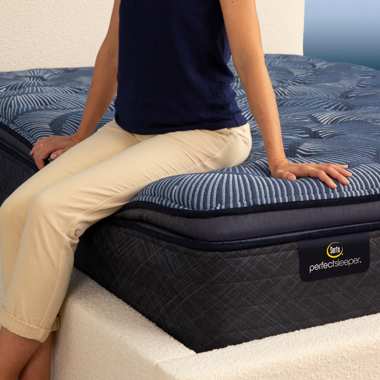 Person sitting on bed to show firmness level of Serta Perfect Sleeper plush pillow top mattress||feel: plush pillow top||level: ultimate