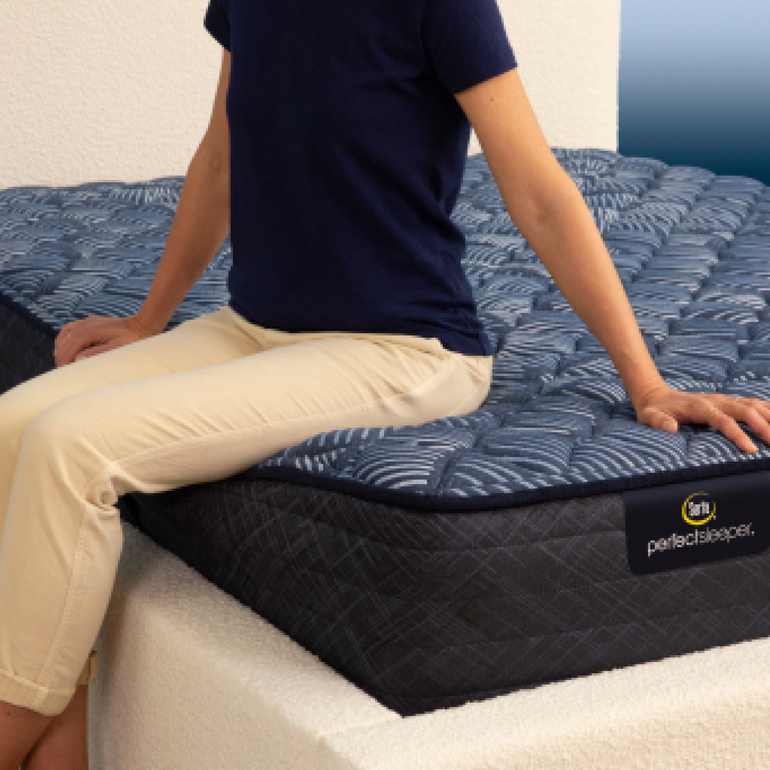 Person sitting on bed to show firmness level of Serta Perfect Sleeper extra firm mattress||feel: extra firm||level: ultimate