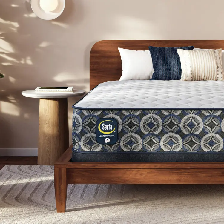 Serta Perfect Sleeper firm mattress on a wooden bed frame with pillows in a bedroom setting
