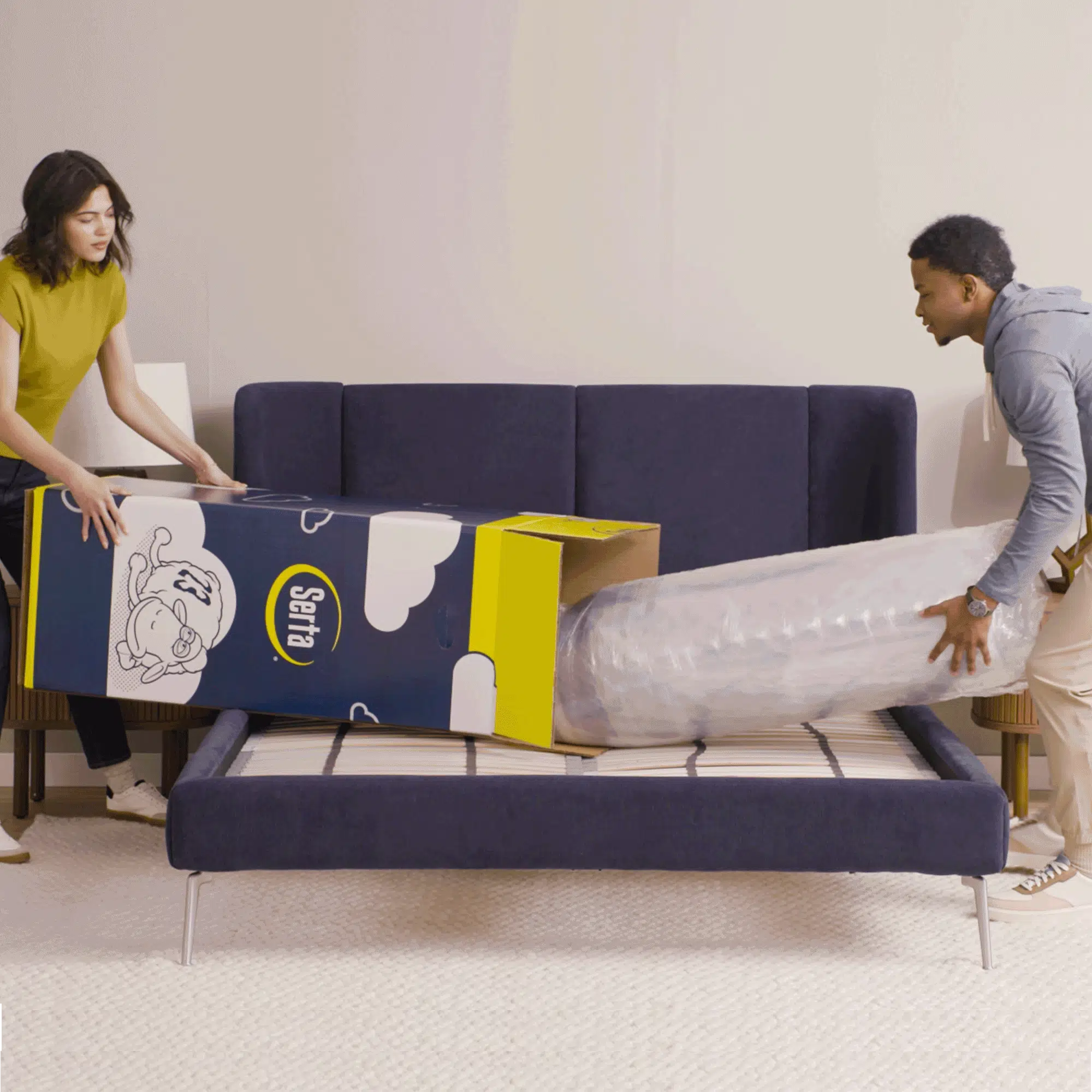 Gif video of a couple opening a mattress in a box, unrolling it and then laying on it.