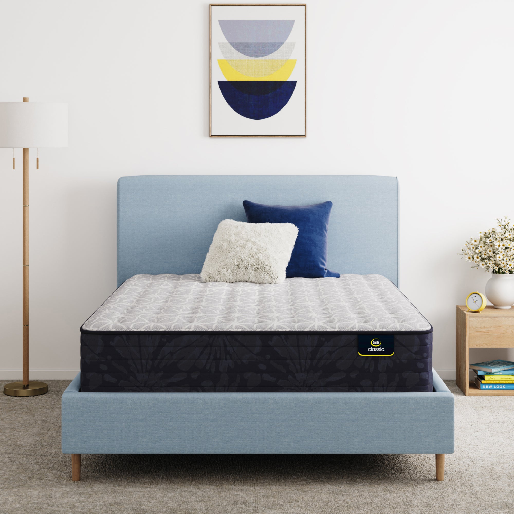Serta Classic Clarks Hill Mattress on a bed with a blue headboard and decorative pillows in a bedroom setting.