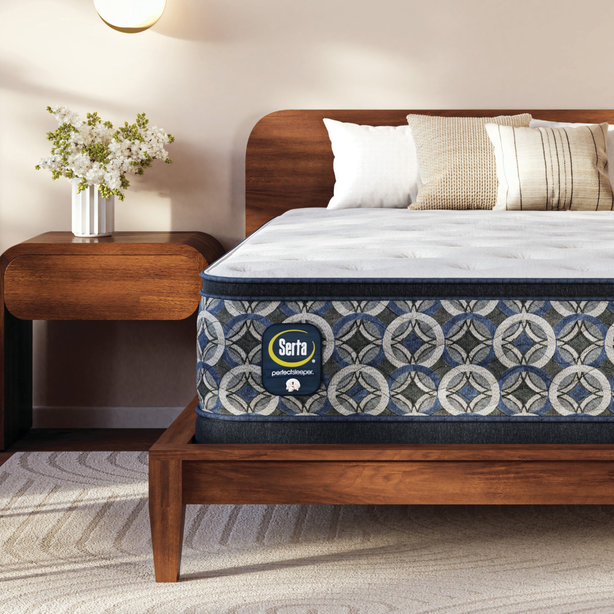 Serta perfect sleeper plush mattress on a wooden bed frame in a bedroom setting with a nightstand and flowers.
